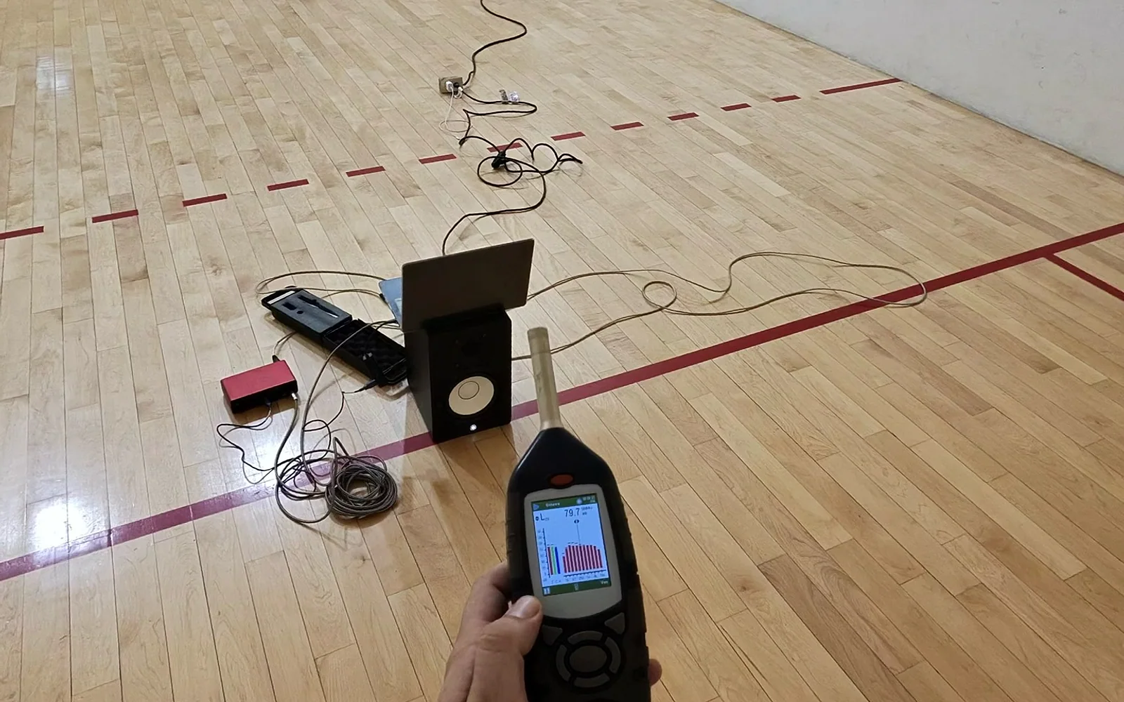 Interior de una cancha de racquet de duela en evaluación acústica, previa a su conversión en salón de danza.
